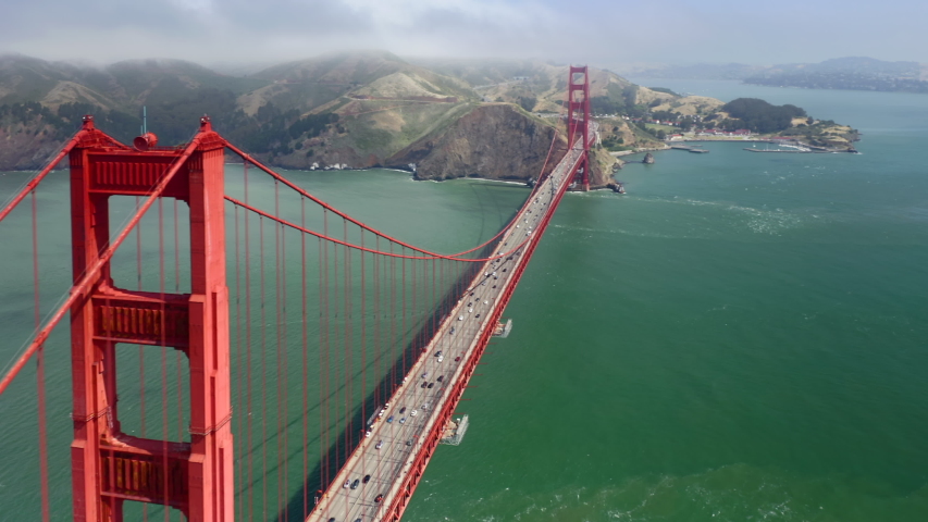 Round going aerial footage observing famous Golden Gate Bridge. Red metal construction against the background of green water of the strait. Amazing collaboration of industrial and natural beauty. 4K Royalty-Free Stock Footage #1042353211