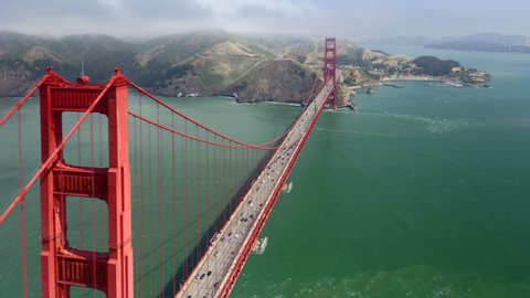 Round going aerial footage observing famous Golden Gate Bridge. Red metal construction against the background of green water of the strait. Amazing collaboration of industrial and natural beauty. 4K