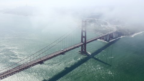 Drone flies high in the sky above floating clouds. Below, overlooks an impressive view of the picturesque Golden Gate Bridge, stretching across the Golden Gate Strait in San Francisco. Aerial. 4K