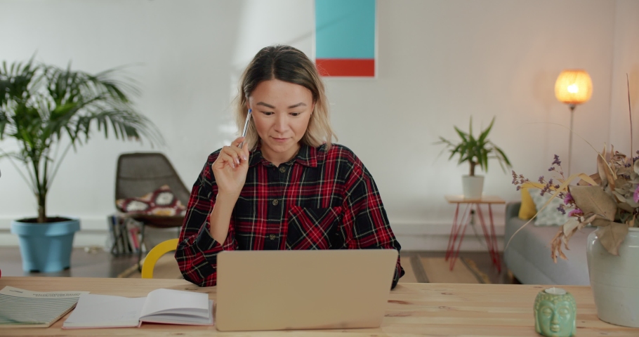 Moment of genial idea coming to mind of nice Asian student using laptop for work at home, concentrated smart female business woman professional freelance working on computer at light living room