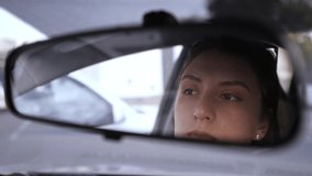 A beautiful Caucasian girl looks in the rear view mirror of the car and puts shadows on her eyes. Violation of the law in the car. A woman gathers in transport