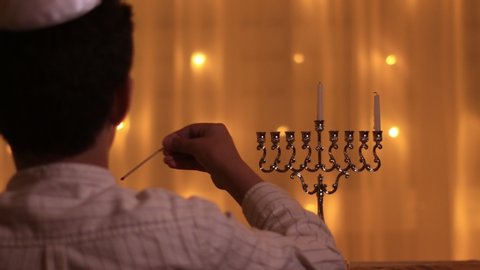 the view from the back of a young boy lights the first candle of the menorah during the Jewish holiday of Hanukkah