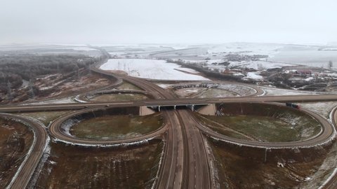 Aerial shot of cars and trucks moving at a winter intersection is a big road junction. Unmanned view of car traffic on a highway in the suburbs in winter. Roundabout at the intersection