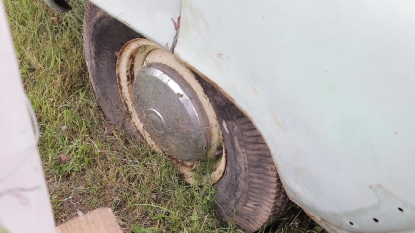 Abandoned broken car covered with dirt and greenery near