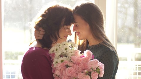 Young adult woman daughter hugging happy middle aged mom, embracing bonding congratulating mature mum with mothers day concept, presenting flowers, celebrating together
