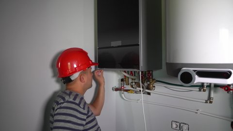 Construction worker man with electric screwdriver mount front panel of gas boiler. Smooth camera motion shot with gimbal.