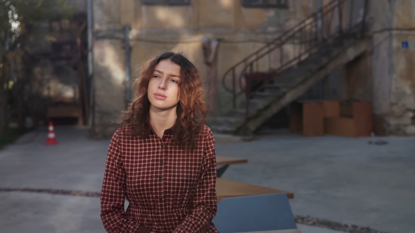 Dreaming young woman with spectacular curly red ginger hair looking at camera posing outdoor in downtown street. Female portrait.