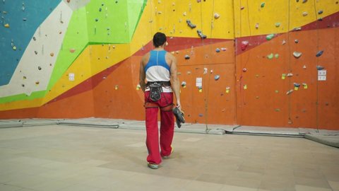 Young man preparing to climb indoor. Practicing rock-climbing on a rock wall indoors