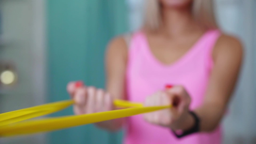Beautiful woman in fashion sporty clothes making exercize with yellow band at home. Concept home workouts