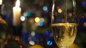 Christmas, New year, Holidays. Bubbles in a champagne glass against a background of candles and flickering colored lights. Background video. Close up.