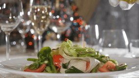 Food video footage in slow motion. Healthy food and vegetarian concept. Closeup shot of pouring olive oil over salad in luxury restaurant with blurred Christmas lights, flashing garland in background