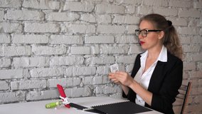 Exposing a blogger, a girl cheating promises to make a lot of money. A woman in a funny business suit and glasses leafs through a folder of documents and talks about millions in kitchen. Copy space