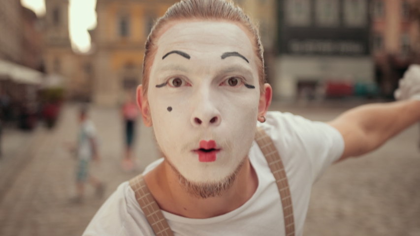 Handsome young mime with beard is performing on street in white makeup. Performer
