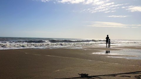 Man and boy on a beach looking at the foamy waves then pointing together at something in the sky. In Spain