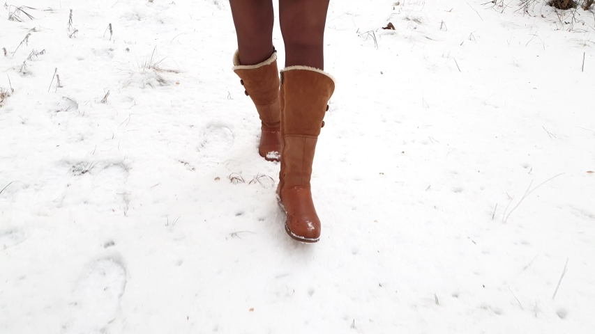 Leg woman winter brown fur boots and pantyhose walking on the snow in a winter park. Closeup outsole of warm boot.