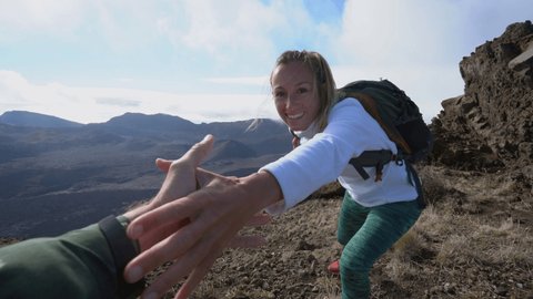 Teammate helping hiker to reach summit. Couple hiking on Hawaiian volcano, hand reach out to help female hiker reach the summit. A helping hand concept