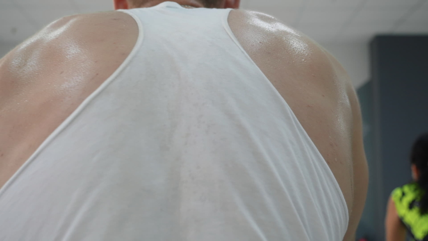 Muscular back of fitness man training on static bike in gym class. Rear view sweating sportsman training on cycling class in fitness club. Cardio training on indoor bike