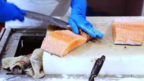 Hands of fishmonger processing fresh raw salmon, preparing fish fillet for sale in shop