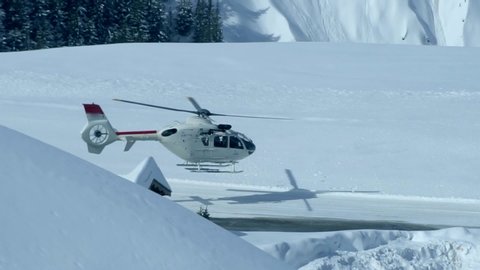 A luxurious white helicopter takes off in the Alpine mountains in winter. Active sports were dropped by a helicopter on top of the mountain. In the background is a mountain range covered in snow.