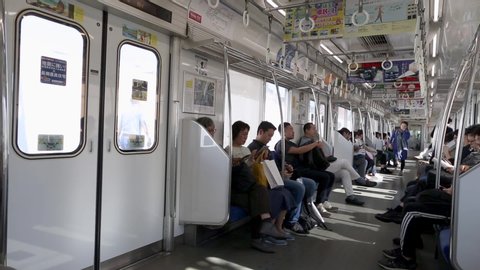 TOKYO, JAPAN - OCTOBER 30, 2019: People are travelling in Tokyo Train to Seibu Shinjuku. People Are Sitting and Playing with Mobile Phones, Reading Books. Train is Approaching to Station.