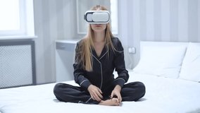 Slow motion young woman use glasses of virtual reality at home sitting on bed look around relaxation vr device entertainment female girl digital experience future relax studio close up