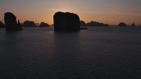 Aerial view above the water during sunrise. Sun rays behind vertical cliffs in Thailand. Sun barely above horizon, warm colors