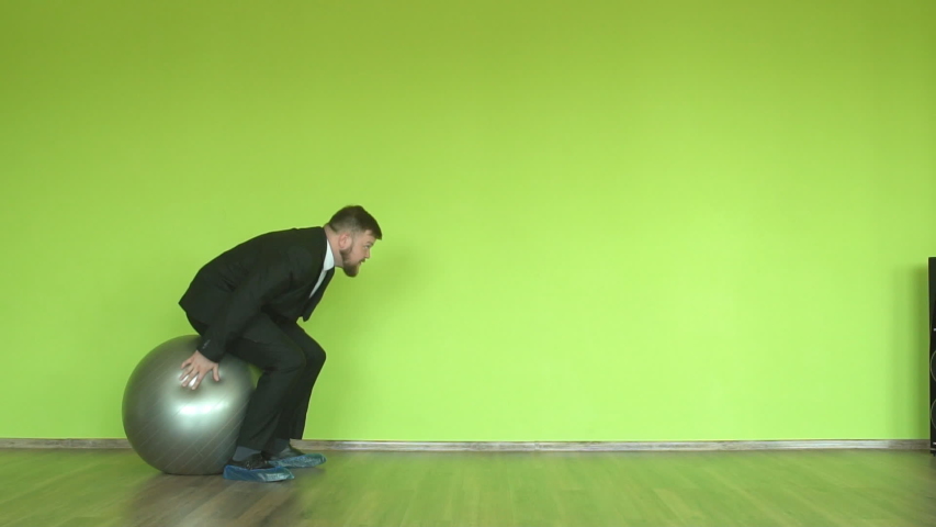 Bearded male office worker jumping on a fitness ball on a green background, chroma key, slow motion