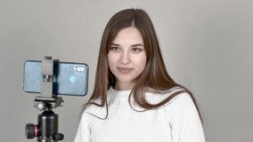 Grey background Caucasian girl blogger white jumper Straight long hair, Standing in front of the phone camera, talking to subscribers, laughing, folding her arms, Close up