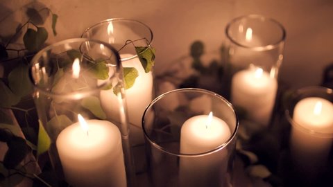 Many large candles burn inside glass glasses. Large, tall wedding candles stand on steps of several levels, burn slowly against background of green leaves. Background relaxation. Beautiful candles.