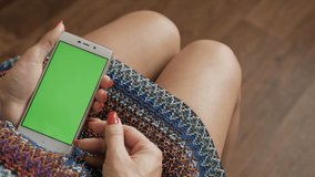 Woman in Skirt Using Smartphone With Green Screen While Sitting in Living Room. Girl POV Scrolling, Typing, Tapping on Touch Screen. Chroma Key. Green Mock-up Screen Smartphone in Vertical Mode.