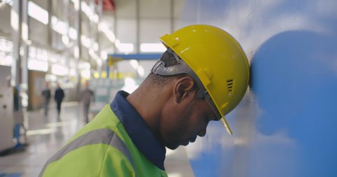 Black industry factory frustrated worker in helmet bangs his head against the wall. Negative upset person lost job and has no money