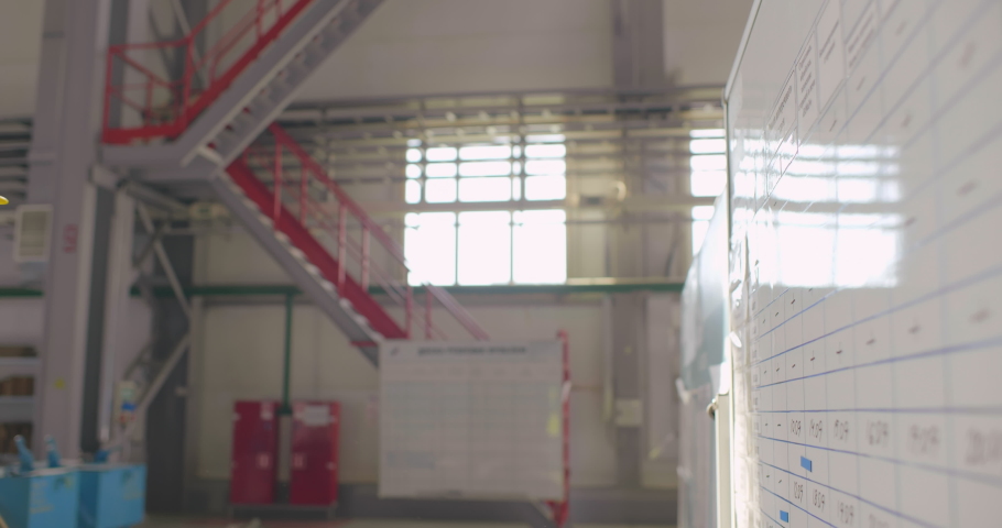 Black industrial worker in uniform looks to a planning board or day schedule, pointing with finger in large factory facility close up. Foreman checks plan of day production in the morning