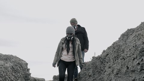 A survivor lovely couple in gas mask going in clouds of toxic smoke on desolate out forest landscape.