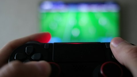 Close view of a gamer's hands playing soccer (football) simulator video game on console using joystick.
