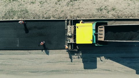 Workers are spreading bitum from the truck. Asphalt paver machine on a road construction site.