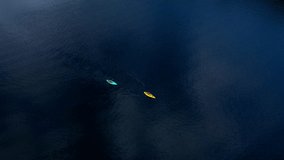 Kayaks paddle on a blue lake from high above. Drone. Ripples on water and cloud reflections contrast with the colorful boats. Good clip for graphics and titles.