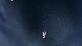 Two canoes paddling on a calm blue lake from high above. Ripples on water and cloud reflections. Good clip for graphics and titles. Drone.
