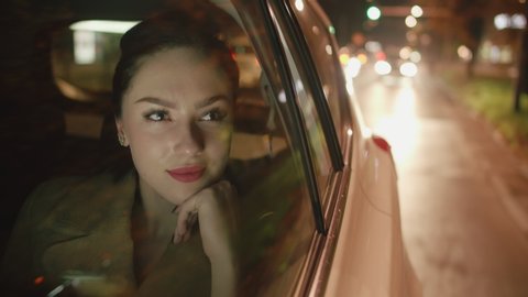 Young smiling woman in the backseat of the car is looking through the window
