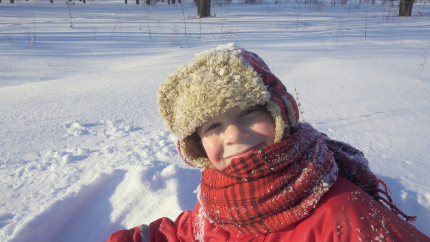 Portrait of happy kid sitting on the snow at winter park, winter outdoor leisures, slow motion