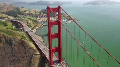 Aerial 4K view over the tower of Golden Gate Bridge in cloudy fog. One of the most attractive for tourists place in United States. Intensive traffic is seen on the bridge. San Francisco, California.