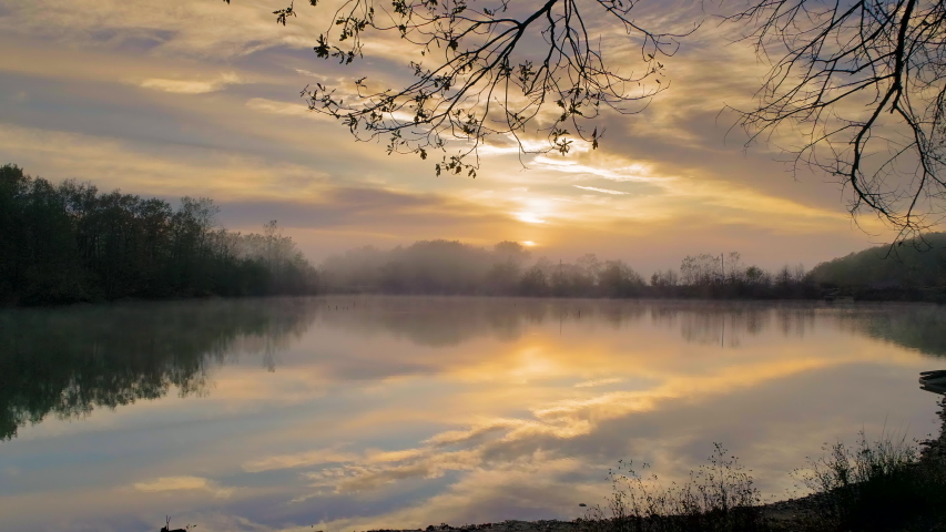 view of misty lake in the early morning. the camera moves over the water to meet the rising sun