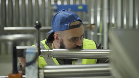 Camera approaching face of serious Caucasian bearded man adjusting steel production equipment. Metal pipes production, steel industry, manufacture.