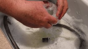 Male hands cleaning CPAP face mask in the sink. Tubing and other mask are in the soapy sink water as the mask is being cleaned.