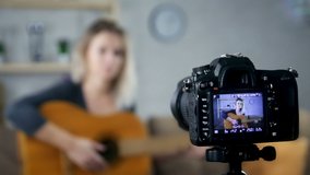 Girl blogger sitting on bed and playing acoustic guitar in front of camera