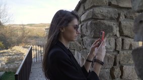 Side view of young beautiful brunette with sunglasses taking photos with and videos with smartphone