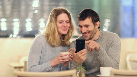 Front view of a funny couple talking about mobile phone content in a coffee shop