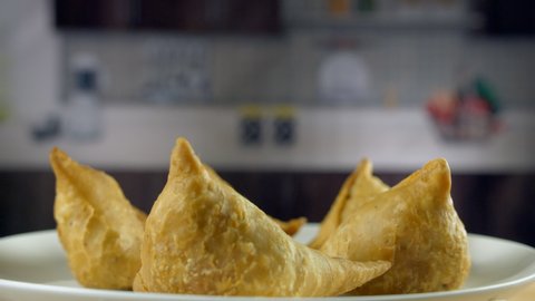 Closeup shot of a samosa plate rotating on a turntable while pouring ketchup - Indian snack. Red tomato sauce poured on yummy and crispy samosas stuffed with mashed potatoes, peas and spices