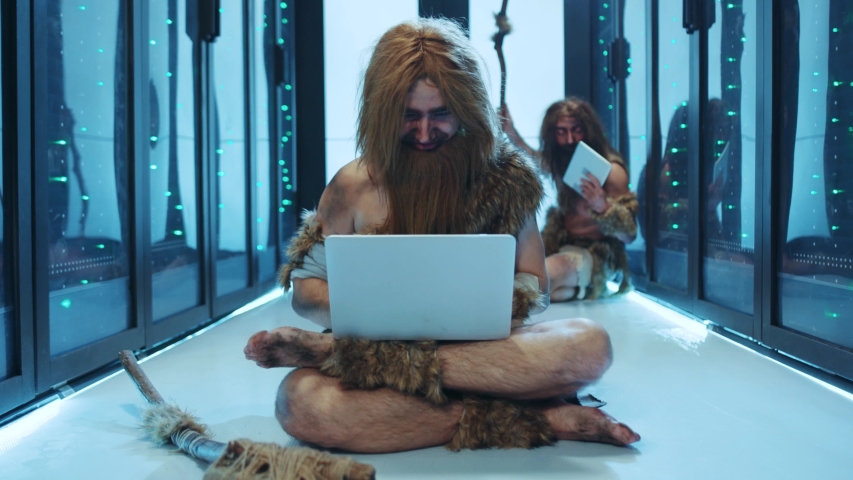 Primeval IT engineer using laptop computer discovering technology at modern database. Happy savage neanderthal dancing with joy having fun staying at data center. Royalty-Free Stock Footage #1042548616