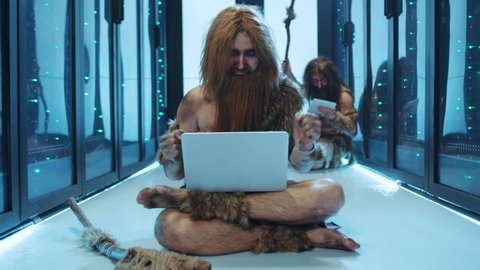 Primeval IT engineer using laptop computer discovering technology at modern database. Happy savage neanderthal dancing with joy having fun staying at data center.