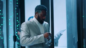 Futuristic african IT engineer using virtual touchpad working on server racks, running backup diagnostics, networking in team at data center. People of future. High technology. - Powered by Shutterstock - Get 15% off with code: PIKWIZARD15